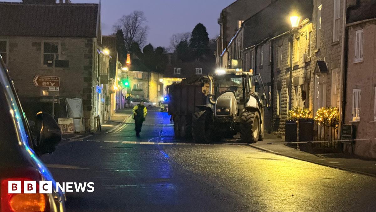 A tractor behind a police cordon on a street. It can be seen to have mounted the footpath