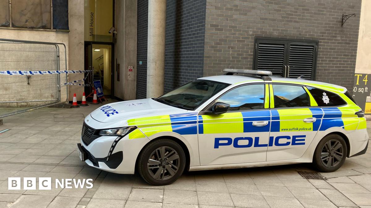 A Suffolk Police car parked in front of a building with blue and white police tape in front of it.
