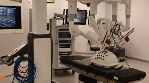 University Hospital of North Tees The white robotic equipment has a long surgical device inserted into a plastic shell on an operating table. 