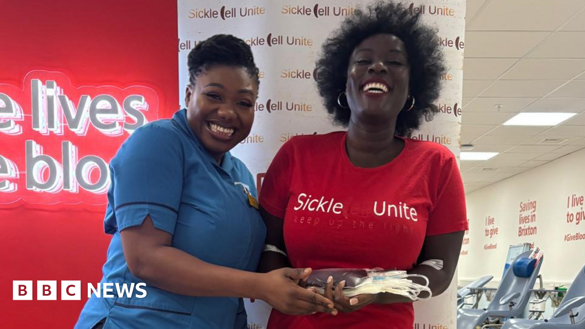 Two women at Brixton blood donation centre. One wears a blue NHS uniform and the other wears a red t-shirt that says: Sickle Cell Unite.