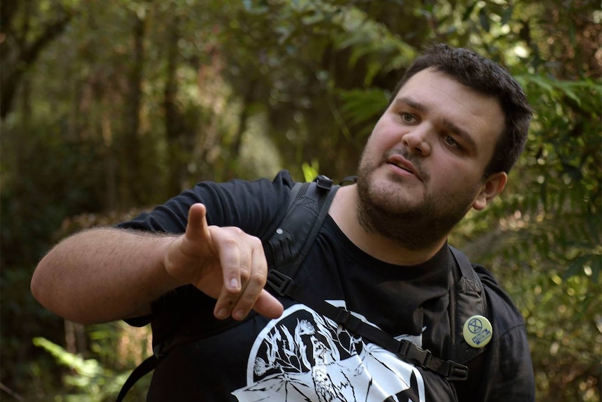 A man wearing a backpack and T-shirt, standing in a forest.