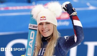 Lindsey Vonn is wearing a white hat with furry ears and holds up her arm