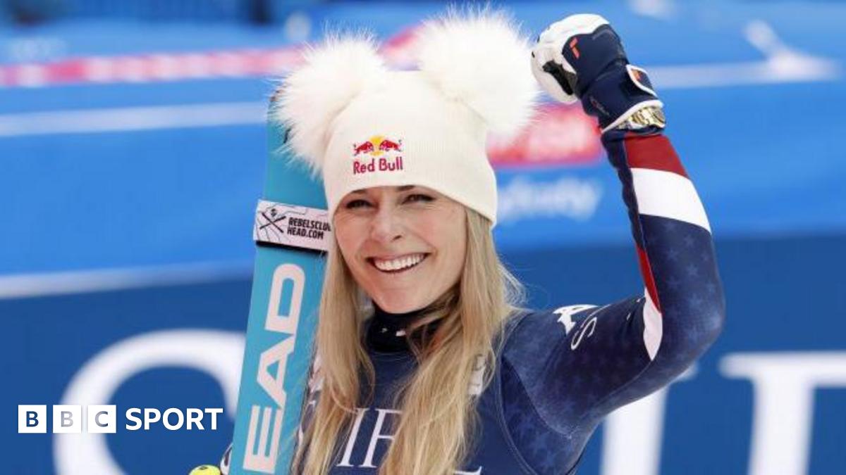 Lindsey Vonn is wearing a white hat with furry ears and holds up her arm