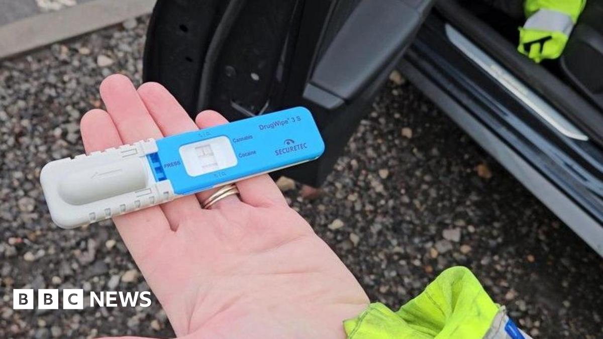 A police officer's hand holding a blue and grey drug testing kit.