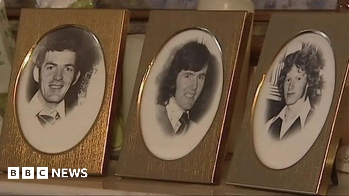 Three individual framed pictures of brothers Anthony, John Martin and Brian Reavey sit on top of  a table. The pictures are black and white. John Martin has short dark hair and is smiling, Brian has long dark hair and is smiling while Anthony has curly, long lighter hair