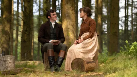 BBC/Bad Wolf/James Pardon Left to right: Mr Hayward (Dónal Finn) wearing a suit in a forest with  Mary Bennet (Ella Bruccoleri), who is dressed in a beige and brown dress.