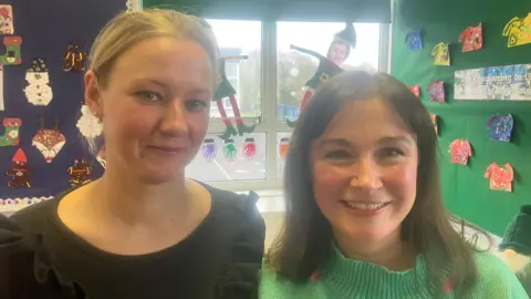 BBC Gillian has a green jumper and brown hair and Gintare has a black top and blond hair. They are in a classroom. 