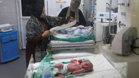 Reuters Palestinian women stand beside a baby receiving treatment inside the neonatal care unit at Nasser Hospital in Khan Younis, southern Gaza (18 December 2025)