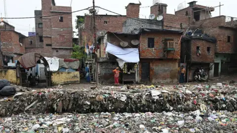 AFP via Getty Images Houses situated along a canal filled with plastic garbage in New Delhi on 8 September, 2024