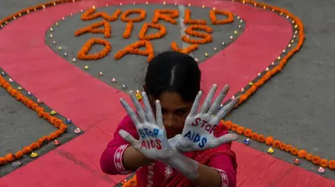 Getty Images A woman dressed in red salwar-kameez shows her palms, with "STOP AIDS" painted on them. The Thalassemia and AIDS Prevention Society organised an awareness demonstration on World AIDS Day in Kolkata, India, on 1 December 2025, to raise awareness about prevention and cure against AIDS in the country