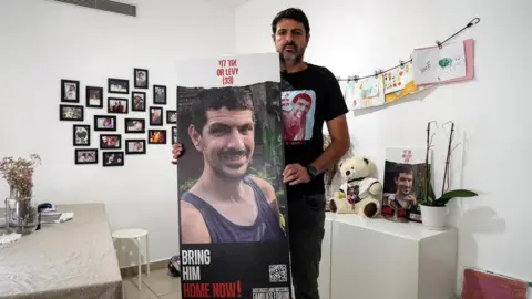 Reuters Michael Levy holds a poster of brother of then-Israeli hostage Or Levy in Ganei Tikva, Israel (17 December 2024)