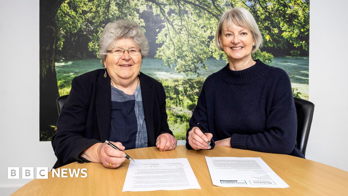 Mary Temperton, leader of Bracknell Forest Council and chair of the Berkshire Prosperity Board, and Liz Leffman, leader of Oxfordshire County Council, posing for a photo as they co-sign the devolutionexpression letter submitted to the government. They are smiling. There is a picture of a park in the sunshine behind them.