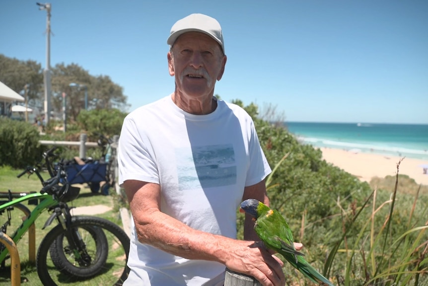 Mr Newton sits on the beach with his rainbow lorrikeet "Kuta".