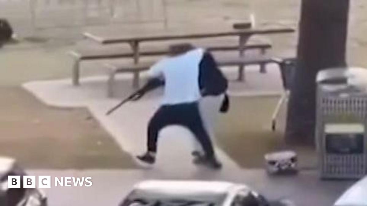 A still image of a man in a white t-shirt tackling a gun from a shooter