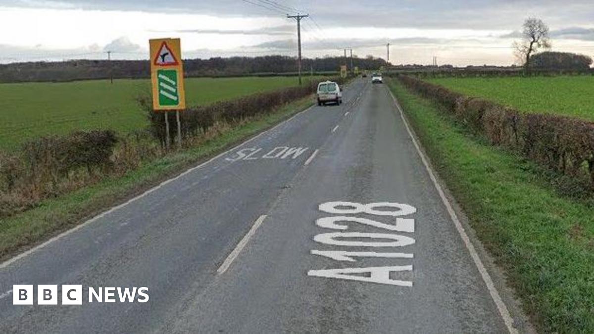 A picture of a road with fields either side. There are two vans in each lane heading in opposite directions.