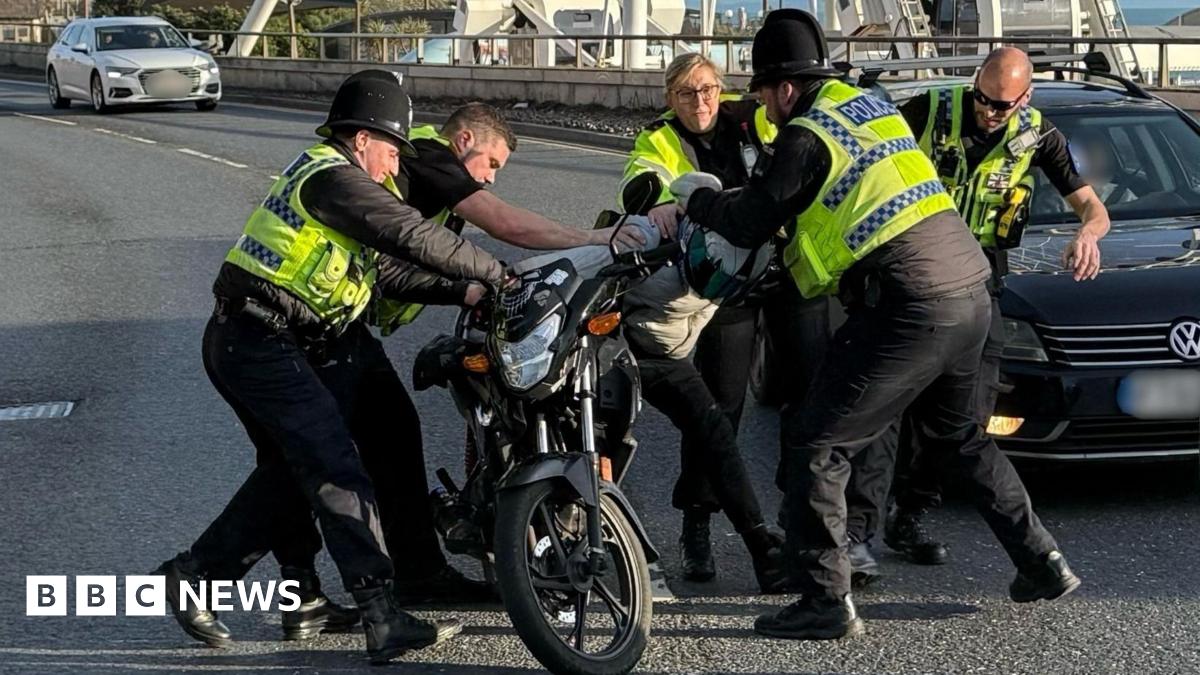 Five police officers appeared to pull a motorcyclist from his bike on a road, with cars passing on the adjoining lane.