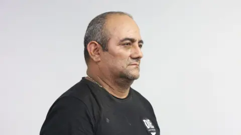 Getty A man in a black T-shirt with a gold chain around his neck poses for a police mugshot.