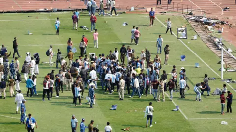 Reuters A large group of football fans stood around on a pitch after invading the field.