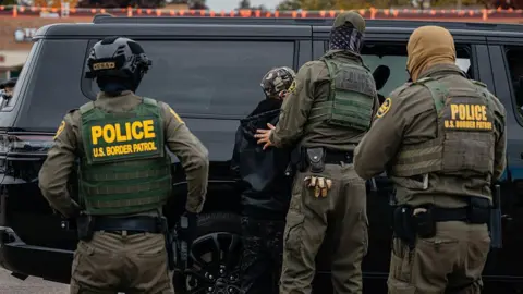 Getty Images Federal immigration agents arrest a man in the parking lot of an H-Mart grocery store on October 31, 2025, in Niles, Illinois. Chief Patrol Agent of the El Centro Sector for U.S. Customs and Border Protection Gregory Bovino was among the agents carrying out the arrest as part of President Donald Trump's administration's "Operation Midway Blitz," an ongoing immigration enforcement surge across the Chicago region.