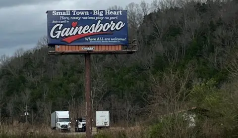 BBC/Mike Wendling A billboard in front of a road which reads: "Small town, big heart, here nasty notions play no part. Gainesboro - where all are welcome."
