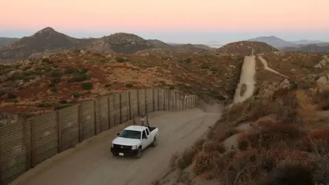 Getty Images A US Border Patrol agent searches for tracks after a night of surveillance using night-vision equipment as agents carry out special operations near the US-Mexico border fence following the first fatal shooting of a US Border Patrol agent in more than a decade on July 30, 2009 near the rural town of Campo, some 60 miles east of San Diego, California. 30-year-old agent Robert Rosas was killed on July 23 when he tracked a suspicious group of people alone in remote brushy hills north of the border in this region. Violence has been escalating in Mexico with fights between well-armed drug cartels and the army becoming common since Mexican President Felipe Calderon began his army-backed war on the cartels. Since the conflict began in late 2006, 12,800 people have been killed. Mexican officials charge that guns which are easily smuggled in from the US have flooded into Mexico where gun laws are strict.