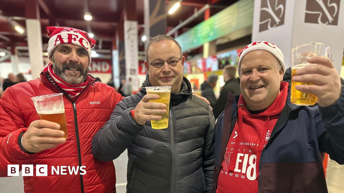 Three men, two of them wearing AFC hats raising a glass a beer inside a football stadium