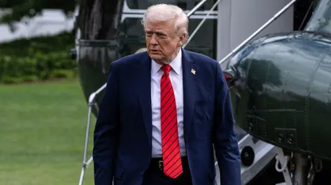 Getty Images Donald Trump walks away from a helicopter wearing a suit and red tie after he returns to the White House following a visit to Walter Reed National Military Medical Center on 10 October 2025.