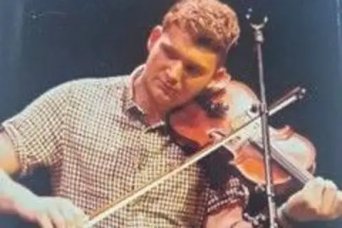 Police Scotland A man in a checked shirt plays the fiddle