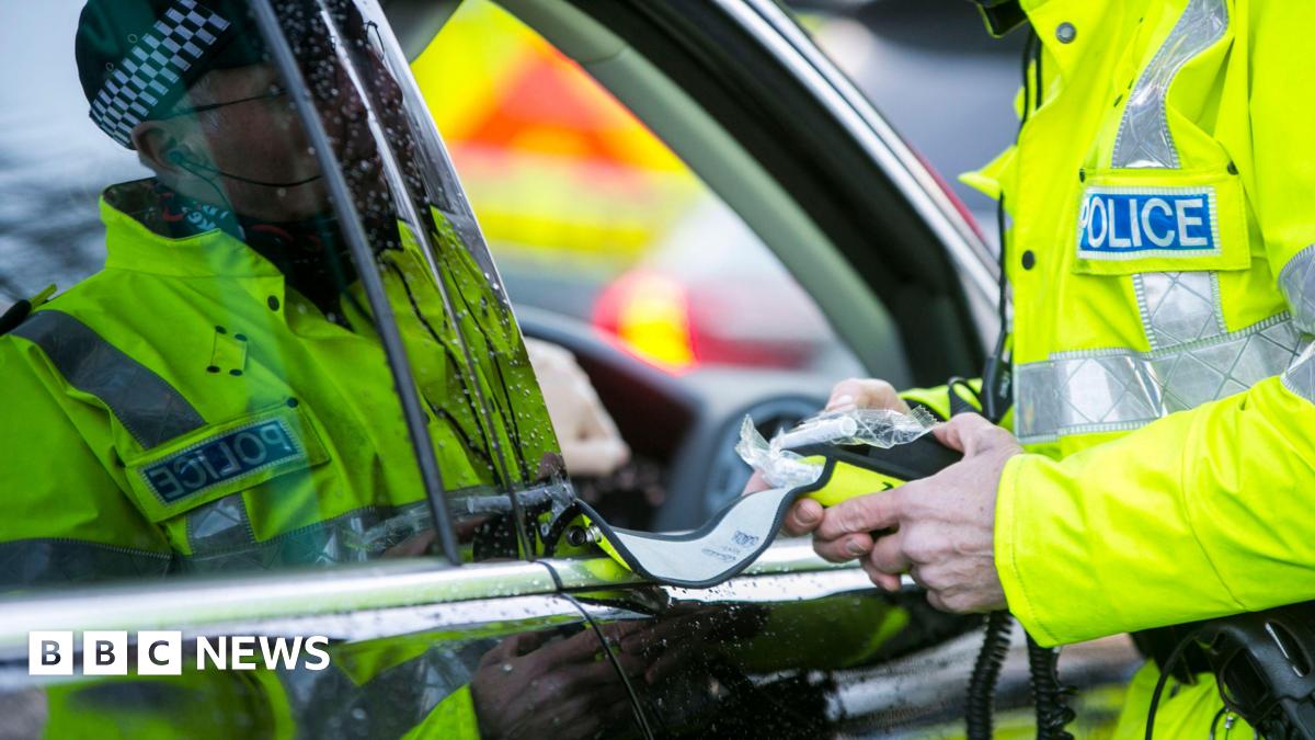 A police officer preparing a breathalyser test as he stands at the side of a driver's car window.