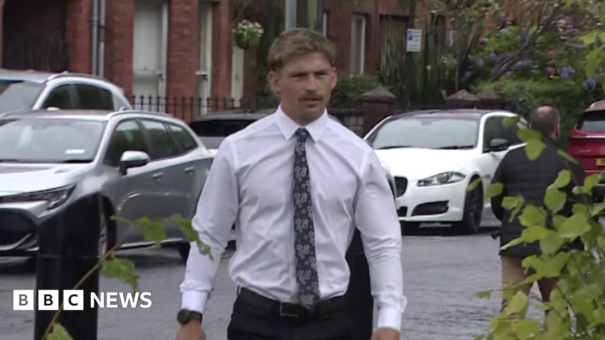 Kavan Keenan is a young man with short blonde/ brown hair and a moustache. He is walking towards the gates into the court as the picture is taken. He is wearing a white long sleeve shirt and a black patterned tie. Behind him is a silver car and two white cars parked along the street in front of red brick terrace houses.