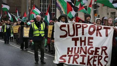 Getty Images A large crowd of protesters carrying Palestinian flags with a row at the front holding a large white banner which reads 'support the hunger strikers' in red lettering.