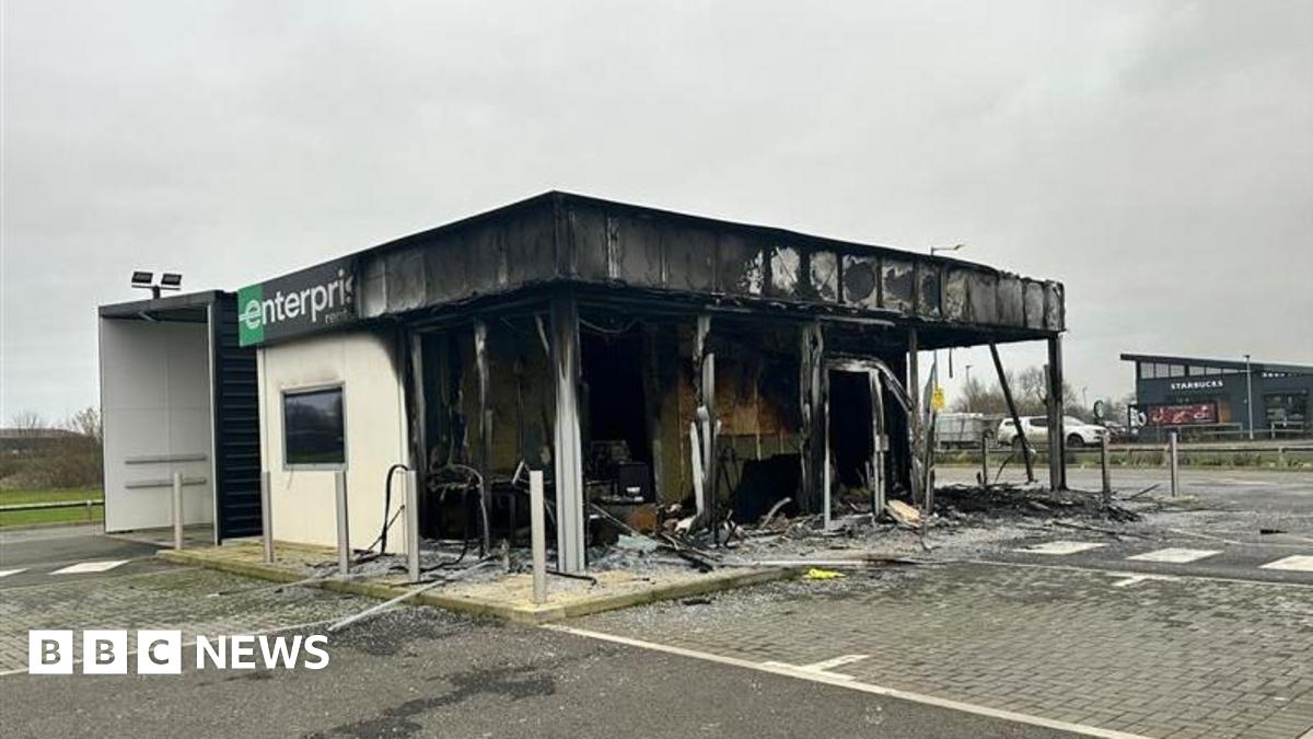 A badly burnt out shell of a building with a car park to the front.