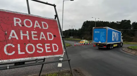 Jack Maclean/BBC A police car with flashing lights parked across a dual carriageway which has been blocked off to traffic by orange cones.