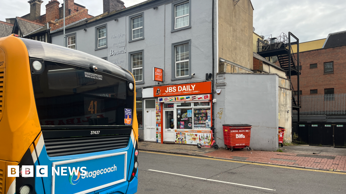 A street with an orange and blue Stagecoach bus. On the other side of the road is a convenience store.