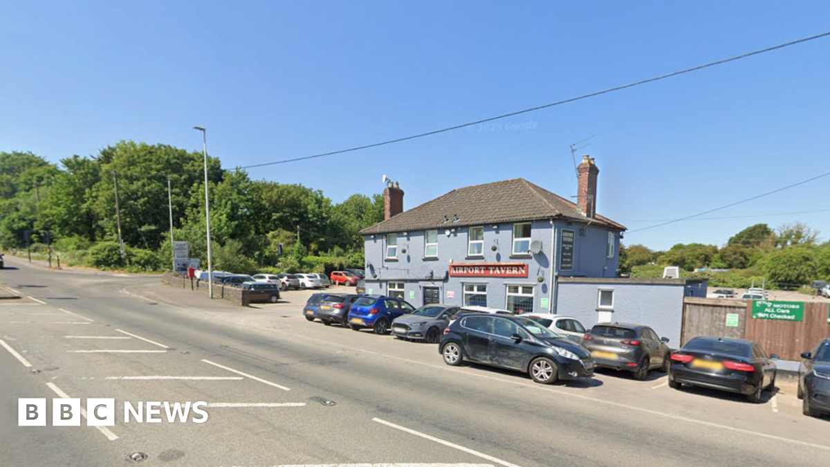 A road outside a blue pub called the Airport Tavern. There are green trees behind the pub and a blue sky. The road is clear.