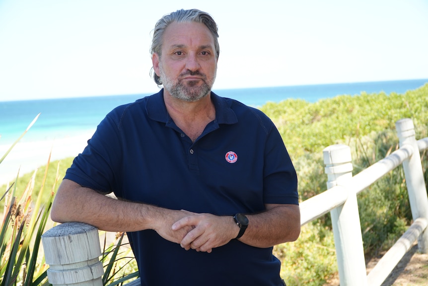 Chris leans on a wooden fence at the beach