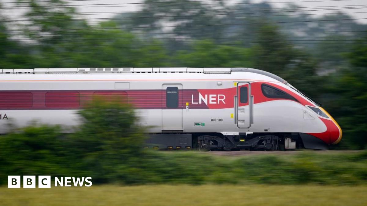 A high-speed train, with a sleek, streamlined front cab, passing through countryside. It is a red and white and says LNER on the side. Green grass and trees and electricity lines look blurred in the background, demonstrating the speed at which the train is travelling.