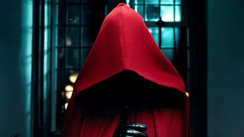 A figure wearing a red cloak on a teaser for The Traitors