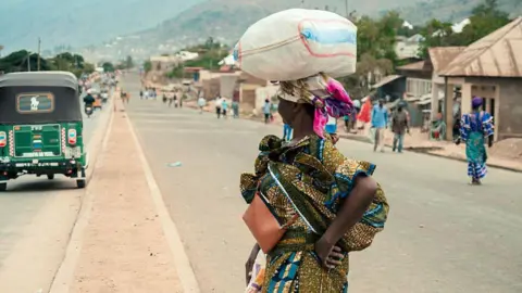 AFP via Getty Images A woman balances a sack of on her head as she crosses a road in Uvira