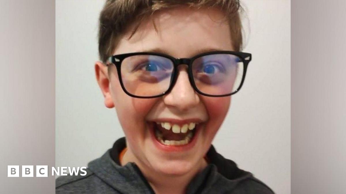 Kyle Sieniawski, laughing. Kyle has a huge smile, large black-rimmed glasses and wears a grey hooded top.