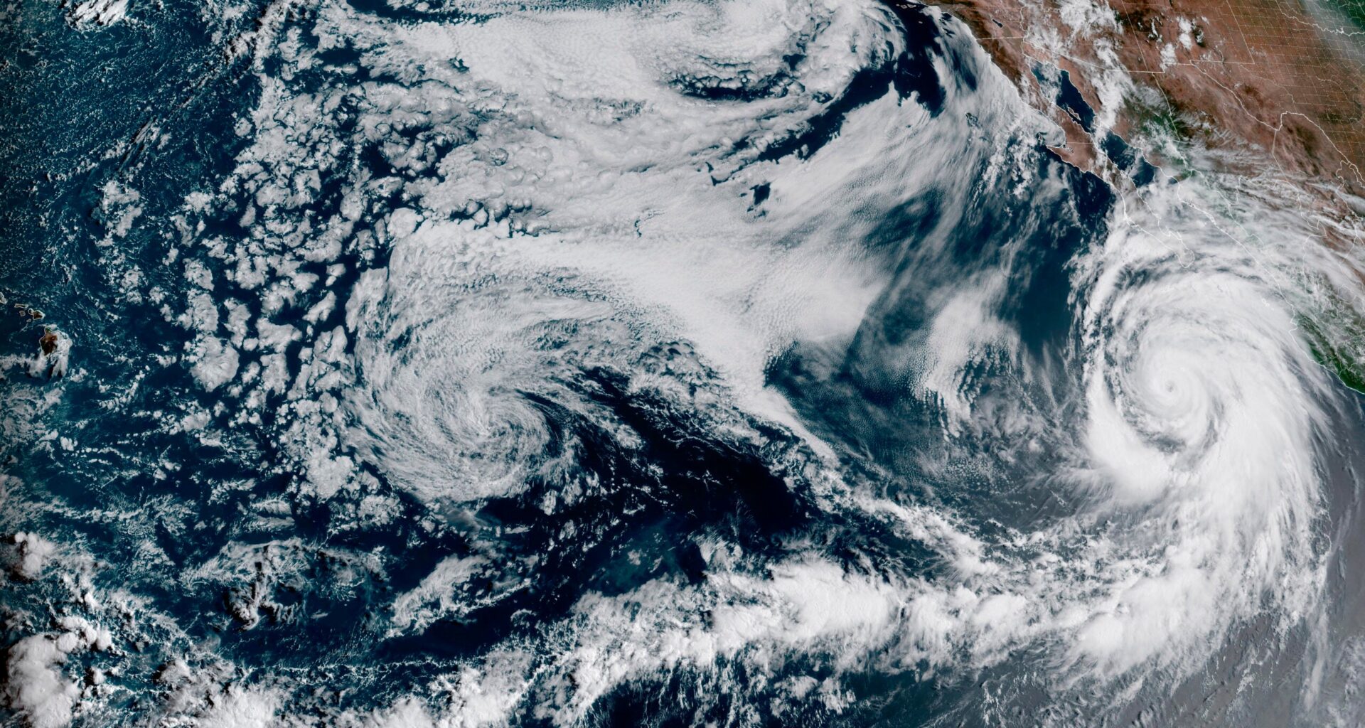 Satellite image showing a large hurricane with a defined eye over the Pacific Ocean, approaching the coast, with swirling cloud formations covering a wide area.