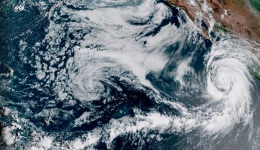 Satellite image showing a large hurricane with a defined eye over the Pacific Ocean, approaching the coast, with swirling cloud formations covering a wide area.