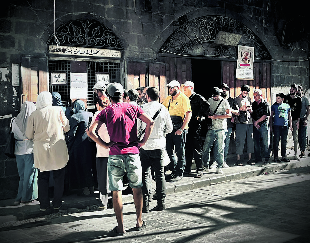 People wait in line outside a government-subsidized bakery in Damascus. Long queues for basic goods remain common as Syria’s economic crisis deepens 