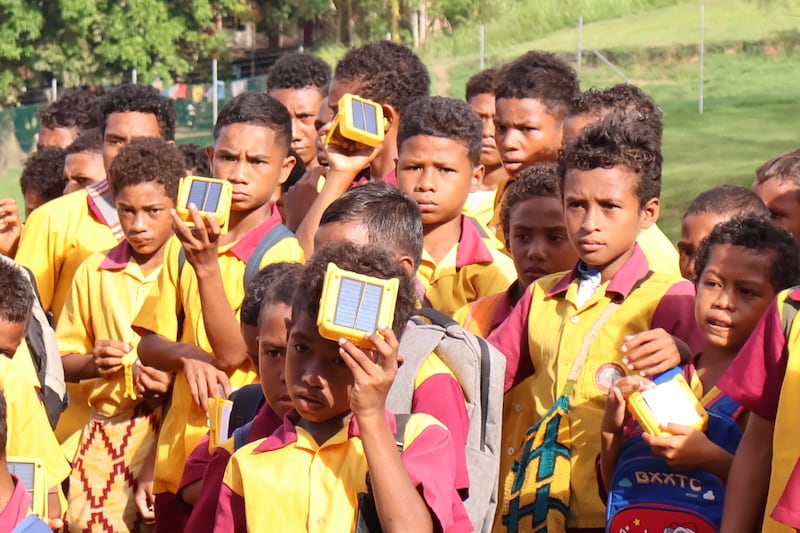 Students of Gavuone Primary School in Gavuone, Papua New Guinea, charge their Solar Buddy lights by holding the solar cells towards the sun on April 15, 2025.