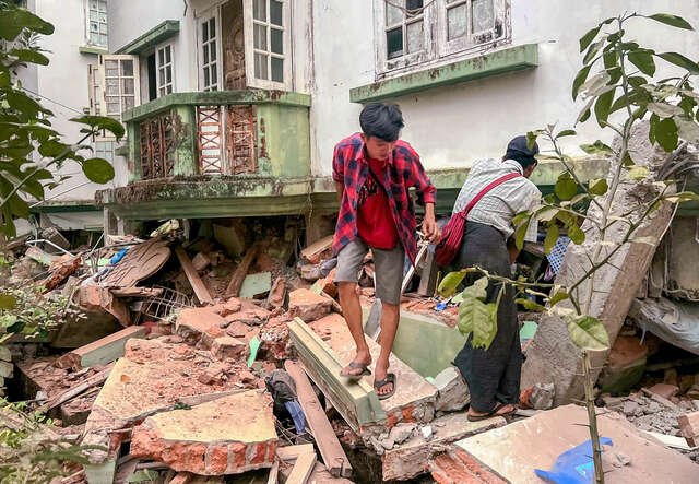 Two people sift through the ruins of a home in Myanmar.