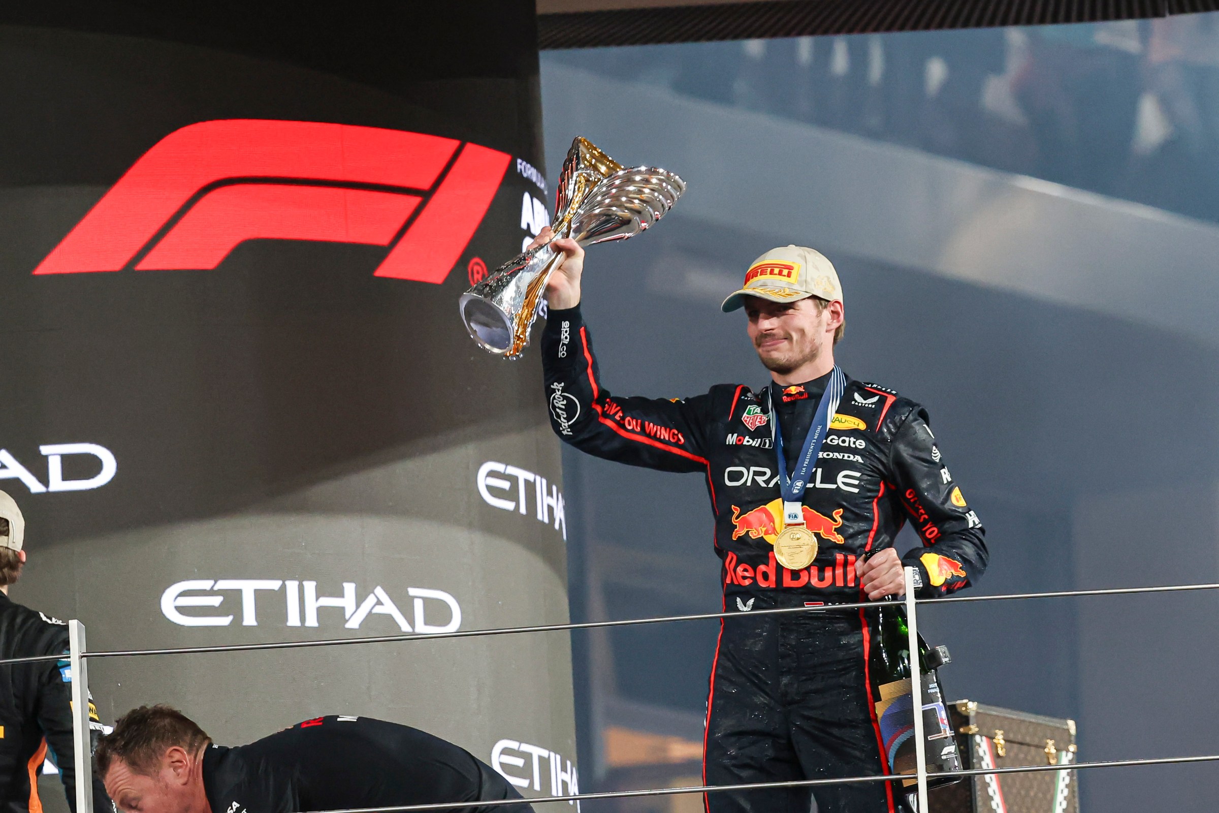 A man holds a trophy and has a medal around his neck, with Redbull costuming for an F1 race