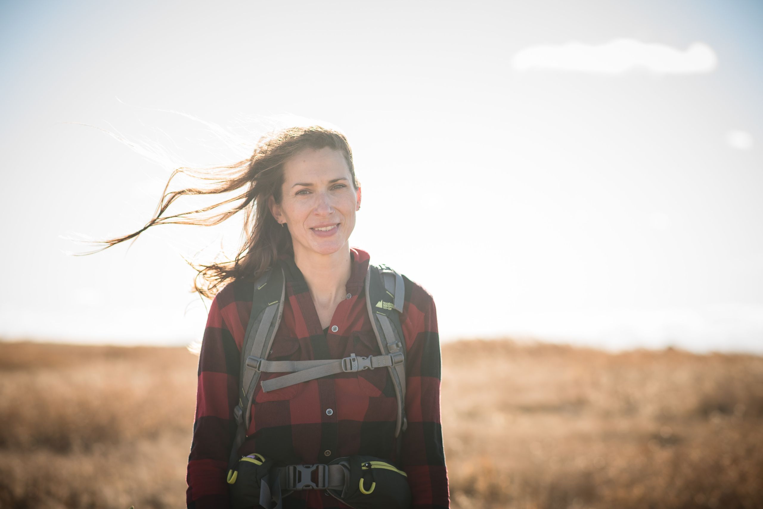 A portrait of Katie Morrison, executive director of the Canadian Parks and Wilderness Society’s southern Alberta chapter, wearing a backpack and red plaid shirt in the prairies