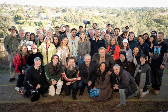The cast and crew of Neighbours filming scenes on location in the countryside. Lucinda Cowden, who plays Melanie, wears a fluorescent green jacket.