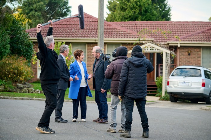 Stefan Dennis, Jackie Woodburne and Alan Fletcher stood on Neighbours' filming location with camera crew around them