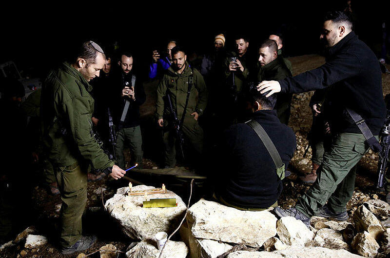 An Israeli soldier lights candles as soldiers gather to celebrate the first day of Hanukkah, near the Israeli-Lebanon border